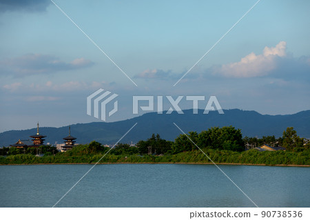 Yakushiji Temple illuminated by the setting sun against the backdrop of Mt. Wakakusa and the summer sky Yakushiji Temple illuminated by the setting sun against the backdrop of Mt. Wakakusa and the summer sky 90738536