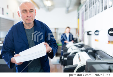 Portrait of an employee of printing house with stack of paper in his hands Portrait of an employee of printing house with stack of paper in his hands 90741963