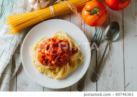 Delicious homemade Spaghetti pasta with tomato sauce and minced meat served on a white plate with ingredient on white wooden background. Italian food. Homemade food. 90746361