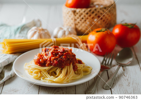 Delicious homemade Spaghetti pasta with tomato sauce and minced meat served on a white plate with ingredient on white wooden background. Italian food. Homemade food. 90746363
