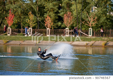 Wakeboarder surfing on lake. Young man surfer having fun wakeboarding in the cable park. Water sport, outdoor activity concept. Wakeboarder surfing on lake. Young man surfer having fun wakeboarding in the cable park. Water sport, outdoor activity concept. 90746567
