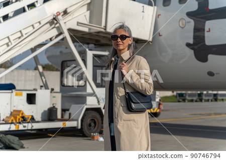 Woman passenger in sunglasses standing outdoors at airport near plane during boarding Woman passenger in sunglasses standing outdoors at airport near plane during boarding 90746794