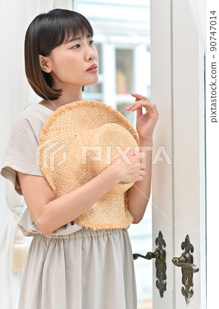 A young woman looking out the window with a straw hat 90747014