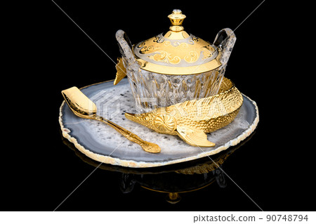Gilded luxury crystal caviar bowl on stand made of natural quartz, carved brass fish figurine and set of shot glasses, dessert spoon on a black background. Gilded luxury crystal caviar bowl on stand made of natural quartz, carved brass fish figurine and set of shot glasses, dessert spoon on a black background. 90748794