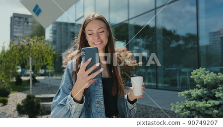 Girl walking with smartphone and coffee cup. Beautiful woman using phone with takeaway coffee on street. Girl walking with smartphone and coffee cup. Beautiful woman using phone with takeaway coffee on street. 90749207
