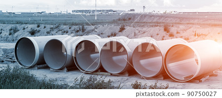 Stack of big frp composite fiberglass plastic sewage pipes at warehouse construction site near Leipzig Halle airport against blue sky background. Highway road construction infrastructure earthworks 90750027