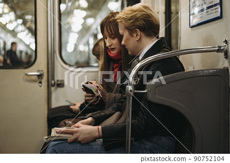 young caucasian women sitting in subway carriage looking at smartphone. Image with selective focus, toning and noise effect young caucasian women sitting in subway carriage looking at smartphone. Image with selective focus, toning and noise effect 90752104