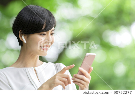 年輕女子在她的智能手機上聽音樂 年輕女子在戶外操作她的智能手機 90752277