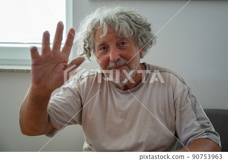 Senior man waving with his man towards the camera Senior man waving with his man towards the camera 90753963