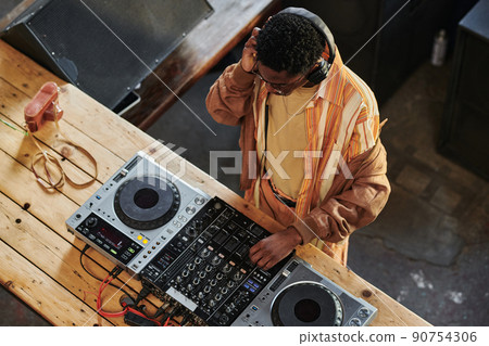 African American guy with headphones mixing sounds on dj set in studio 90754306