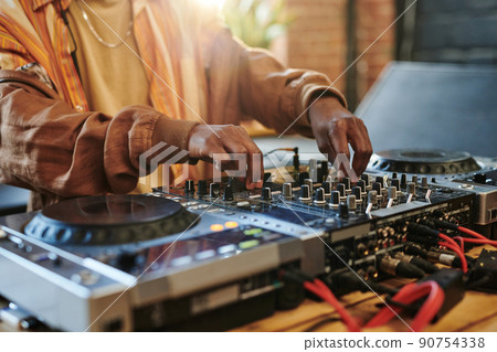 Hands of black man regulating sounds on dj set while turning mixers 90754338