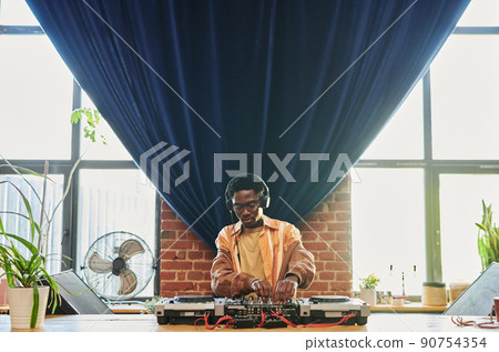Young man in headphones and casualwear standing by table with dj set 90754354