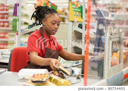 Young black woman in uniform scanning packed food products of buyers Young black woman in uniform scanning packed food products of buyers 90754403