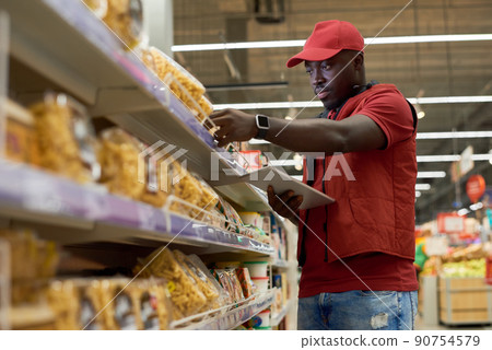 Young male shop assistant in uniform checking prices of packed chakchak 90754579