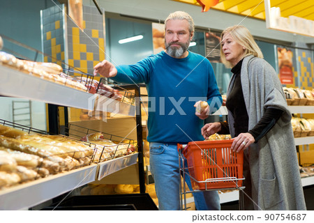 Aged man and his wife in casualwear choosing fresh bread in grocery department 90754687