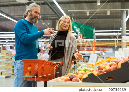 Mature man pointing at display with fresh fruits while choosing apples Mature man pointing at display with fresh fruits while choosing apples 90754689