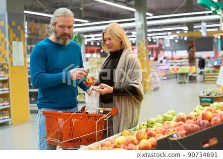 Aged couple choosing fresh ripe apples in grocery department of supermarket Aged couple choosing fresh ripe apples in grocery department of supermarket 90754691