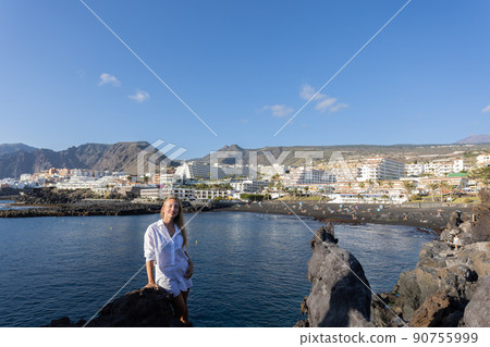 Young smiling woman near volcanic rocks on a city and ocean background. Young smiling woman near volcanic rocks on a city and ocean background. 90755999