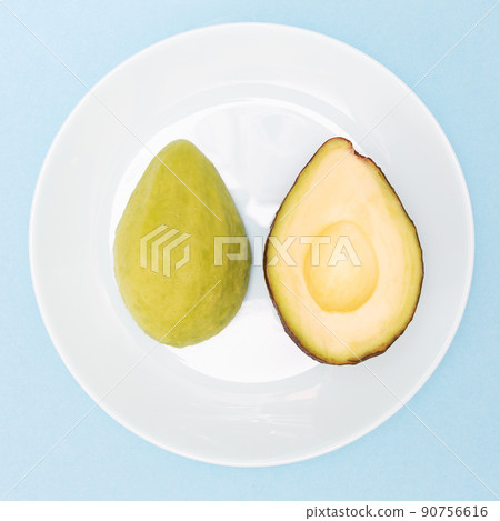 Avocado cut in half, one part without peel. Ripe avocado fruit in a plate on a blue background. Healthy food concept. Flat lay. Top view. Square. 90756616