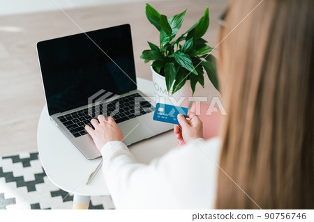 Young woman sitting at desk and using debit credit card for online shopping banking investments on her laptop. Blank copy space mockup laptop screen with the flower in the background 90756746