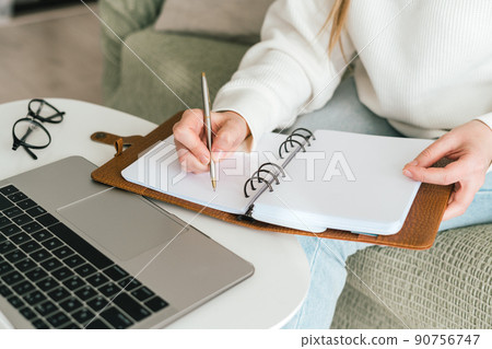 Woman writes in notebook with laptop Woman writes in notebook with laptop 90756747