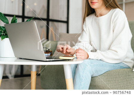 Freelance young woman with mobile cellphone typing at laptop and working from home office with. Happy girl on workplace at desk. Distance learning online education. Taking selfie or video chat. 90756748
