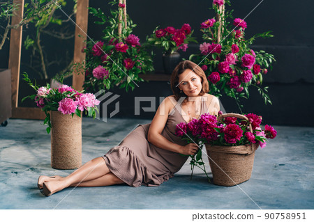a woman sits on a podium near a basket of peonies and collects a bouquet. a woman sits on a podium near a basket of peonies and collects a bouquet. 90758951