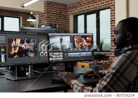 African american creative digital video editor sitting at desk while improving recorded footage visual quality. Professional post production videographer editing graphic content using specialized African american creative digital video editor sitting at desk while improving recorded footage visual quality. Professional post production videographer editing graphic content using specialized 90759254