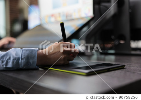 Closeup of creative graphic designer using stylus pen and graphic tablet to edit photos. Digital photo editor sitting at desk with multiple displays while using editing software to retouch images. 90759256