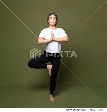 Beautiful young woman working out indoors, doing yoga exercise against green studio wall background Beautiful young woman working out indoors, doing yoga exercise against green studio wall background 90761206