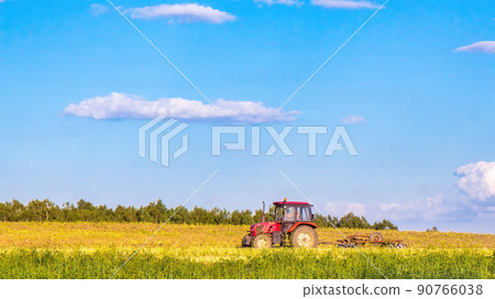 A red tractor plows a field on a summer day. Working day in agriculture A red tractor plows a field on a summer day. Working day in agriculture 90766038