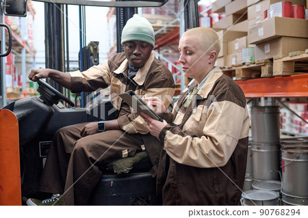 Female manager using digital tablet to show the tasks for forklift driver during their work at warehouse 90768294