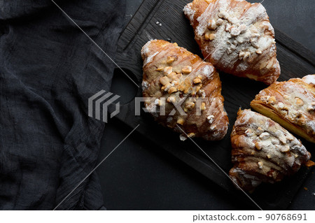 Baked croissant on a wooden board and sprinkled with powdered sugar, black table Baked croissant on a wooden board and sprinkled with powdered sugar, black table 90768691