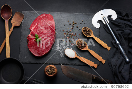 Raw beef tenderloin lies on a cutting board and spices for cooking on a black table Raw beef tenderloin lies on a cutting board and spices for cooking on a black table 90768692