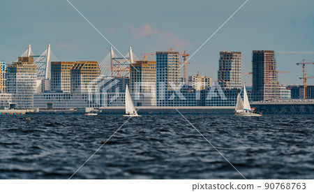 The residential complex under construction on the embankment of the Neva River on Vasilievsky island in sunny day, bulk island, construction cranes, sailing yachts, river navigation 90768763