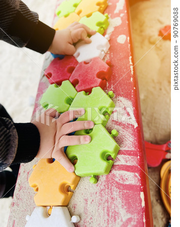 The child plays in the sandbox with colorful puzzles. Selective focus The child plays in the sandbox with colorful puzzles. Selective focus 90769088
