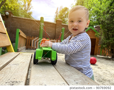 A little cute boy of one and a half years plays with toy car at the playground. Adorable toddler playing with cars and toys outdoor. Family, holiday, kids lifestyle concept. Selective focus A little cute boy of one and a half years plays with toy car at the playground. Adorable toddler playing with cars and toys outdoor. Family, holiday, kids lifestyle concept. Selective focus 90769092