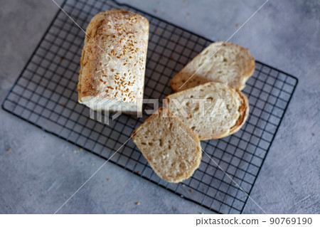 Baked Ruddy Wheat Bread Brick on sourdough with flax seeds on a black grid, on gray concrete background. 90769190