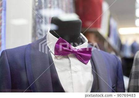 In the shop window is a mannequin in a formal suit and bow tie. In the shop window is a mannequin in a formal suit and bow tie. 90769483