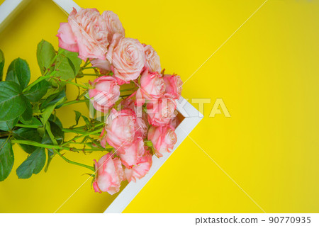 The white frame lies diagonally to the side, inside there is a bouquet of pink roses on a bright yellow background. High quality photo The white frame lies diagonally to the side, inside there is a bouquet of pink roses on a bright yellow background. High quality photo 90770935