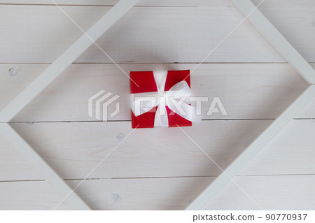 A white wooden frame lies diagonally on a white wooden background, inside it is a red gift box. High quality photo A white wooden frame lies diagonally on a white wooden background, inside it is a red gift box. High quality photo 90770937