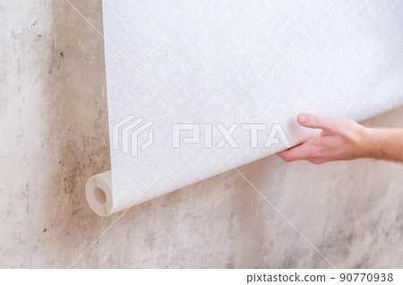 A man rolls out a roll of white wallpaper on the A man rolls out a roll of white wallpaper on the 90770938