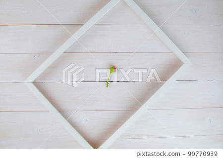 A white wooden frame lies diagonally on a white wooden background, inside it lies a bud of an unopened rose. High quality photo A white wooden frame lies diagonally on a white wooden background, inside it lies a bud of an unopened rose. High quality photo 90770939