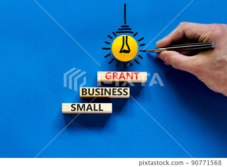 Small business grant symbol. Concept words Small business grant on wooden blocks on a beautiful blue table blue background. Businessman hand. Business, finacial and small business grant concept. 90771568