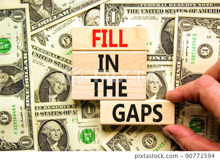 Fill in the gaps symbol. Concept words Fill in the gaps on wooden blocks on a beautiful background from dollar bills. Businessman hand. Business, motivational and fill in the gaps concept. 90771594