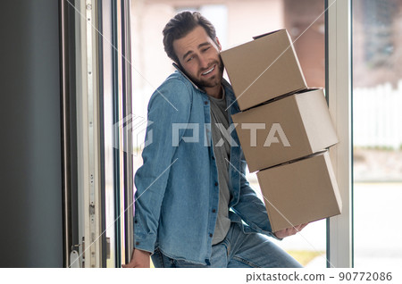 Man talking on smartphone bringing boxes into apartment 90772086