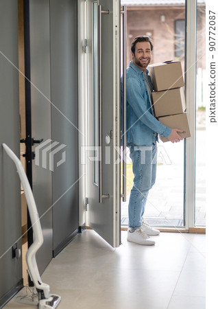 Man with boxes in hands entering house Man with boxes in hands entering house 90772087
