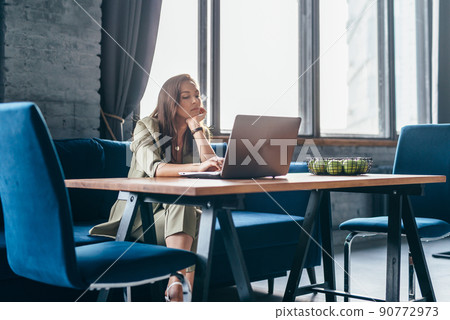 Woman at home sits at her desk and looks at her laptop screen Woman at home sits at her desk and looks at her laptop screen 90772973