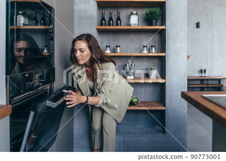 Woman peeks into the oven to check on a baked dish Woman peeks into the oven to check on a baked dish 90773001
