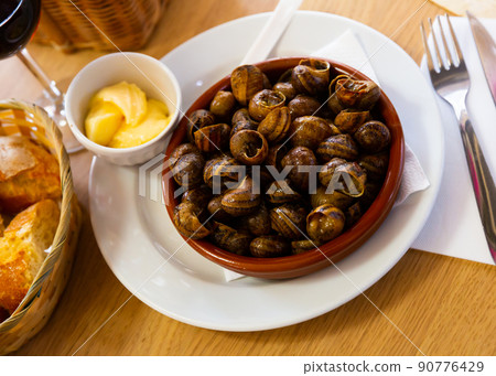 Tasty baked snails in bowl, served with bread and butter Tasty baked snails in bowl, served with bread and butter 90776429